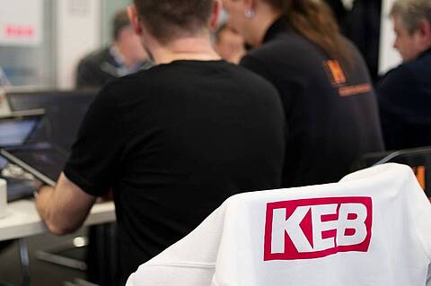 people sitting around a table and working on laptops, in the front is the logo of KEB Automation visible on a white jacket